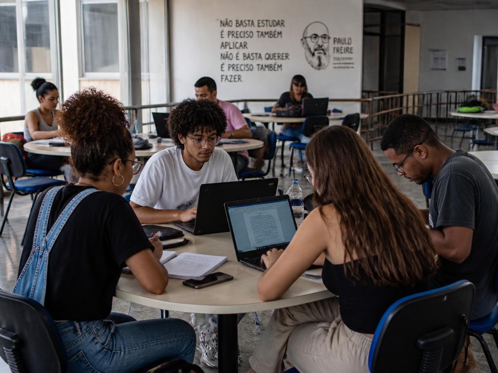 Grupo diverso de estudantes universitários, incluindo mulheres, pessoas negras e jovens, estudando juntos em sala de estudos.